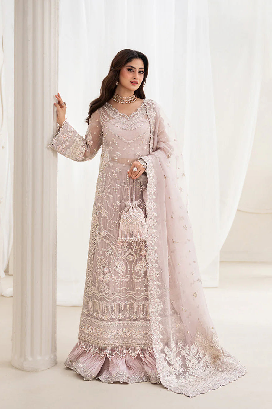 Woman in a light pink embroidered traditional outfit against a white curtain background