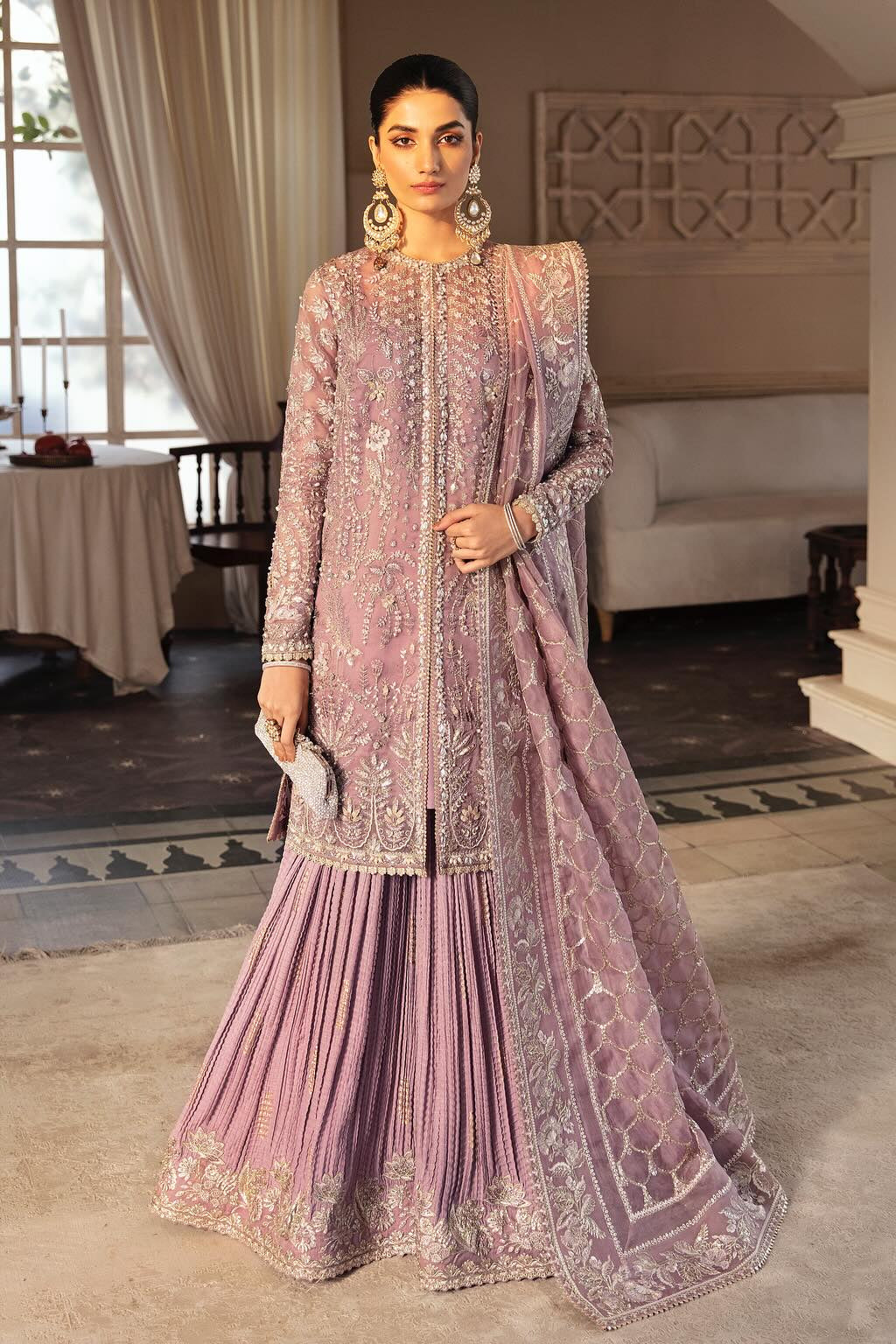Woman in a pink embroidered traditional outfit standing in an elegant room.