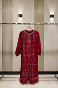 A red long-sleeve embroidered dress displayed on a clothing rack against a beige paneled wall with wall-mounted lights.