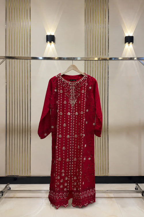 A red long-sleeve embroidered dress displayed on a clothing rack against a beige paneled wall with wall-mounted lights.