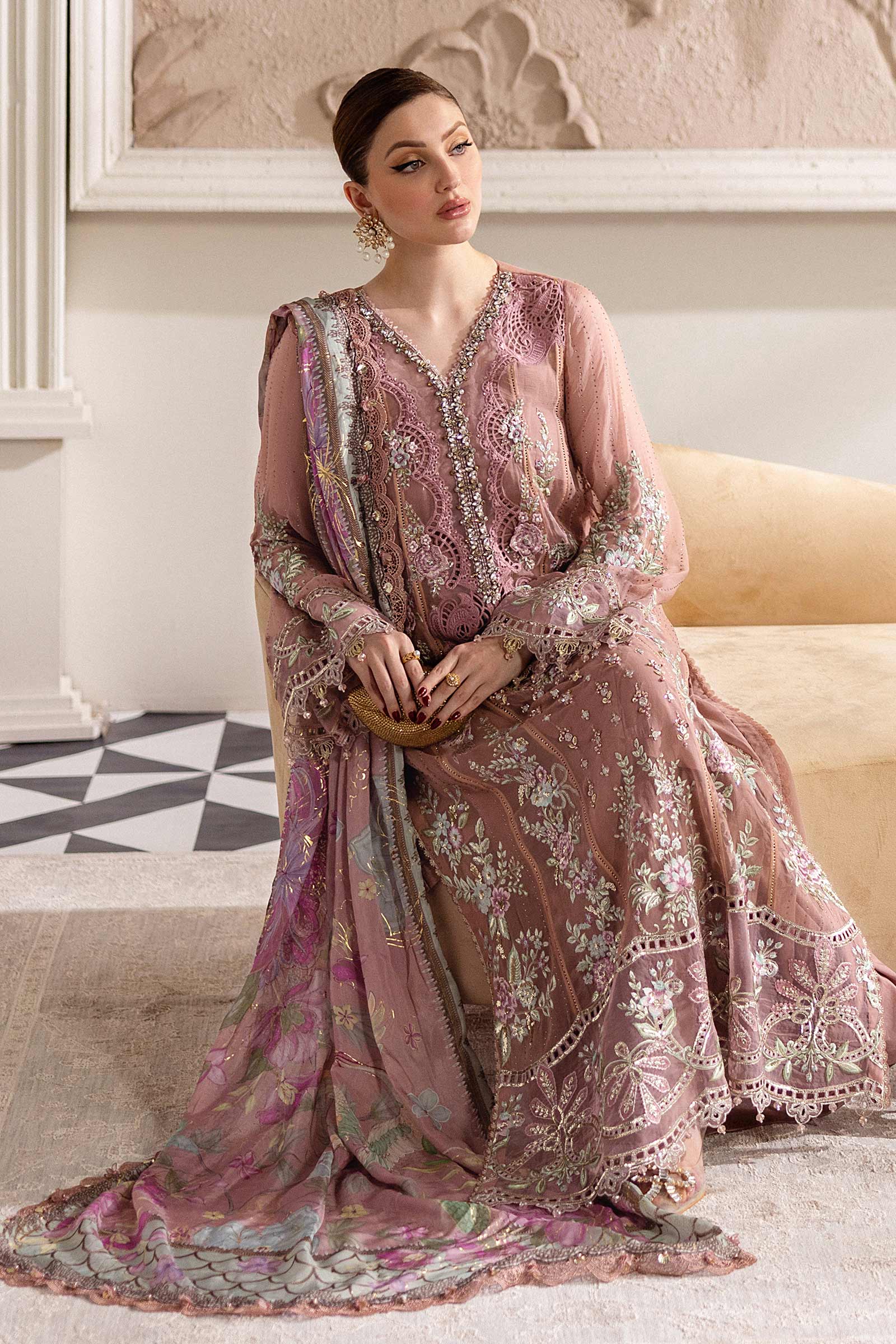 Woman in a pink embroidered dress sitting on a couch in a decorated room.