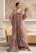 Woman in a pink embroidered traditional outfit standing in a decorated room.