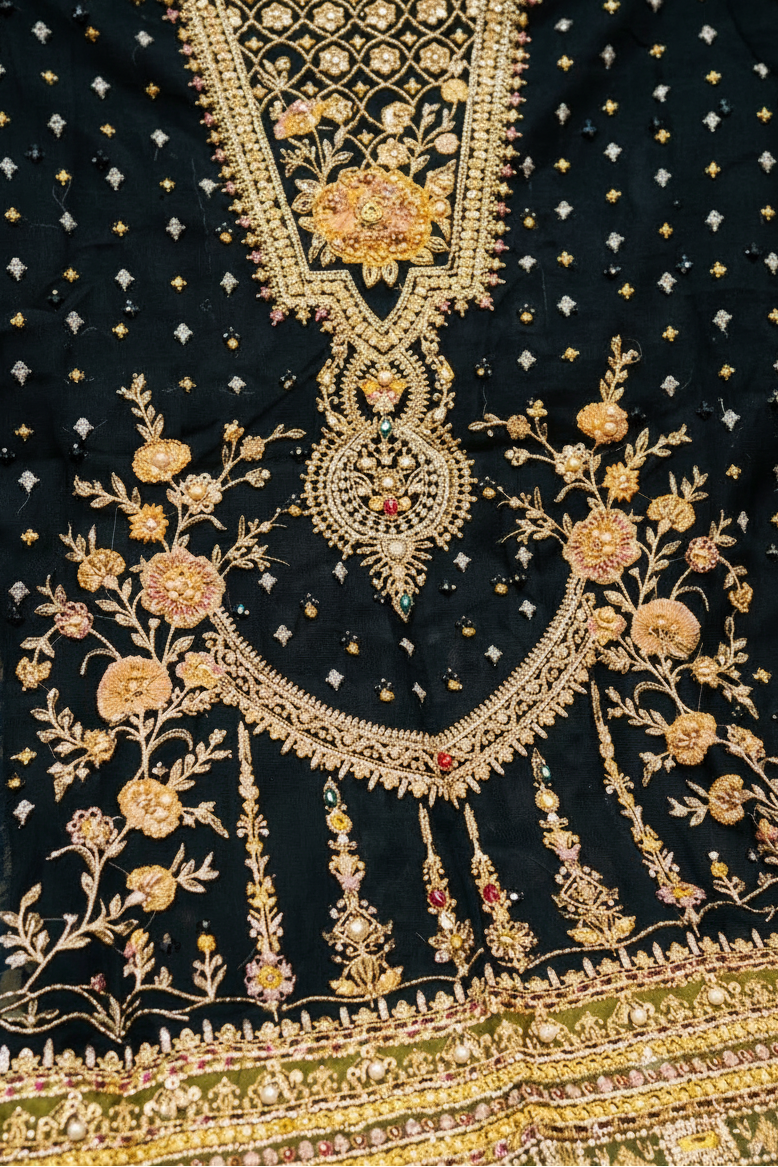 Black cotton fabric with intricate gold and beige floral embroidery, metallic zari work, and small gold star motifs, featuring a heavily embellished neckline and border.