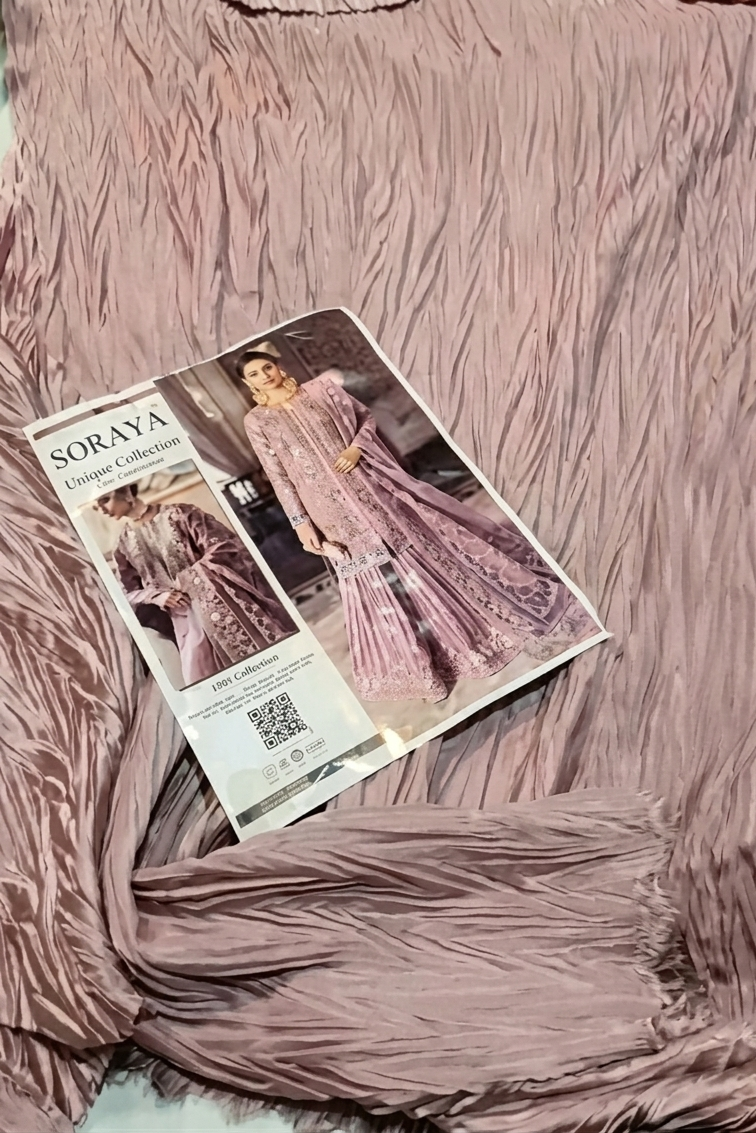 A mauve-colored, heavily textured fringed fabric is draped across the frame, with a printed fashion catalog page titled 'SORAYA Fashion Collection' placed on top.