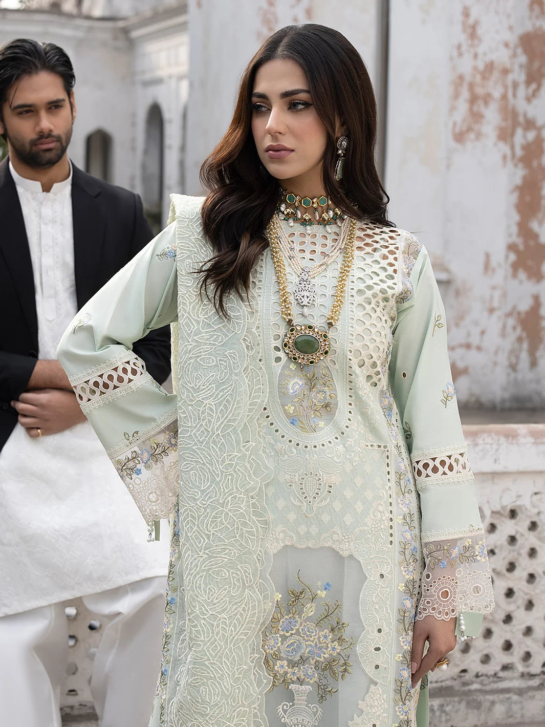 Woman in a light green embroidered traditional outfit with a man in a white kurta in an outdoor setting.