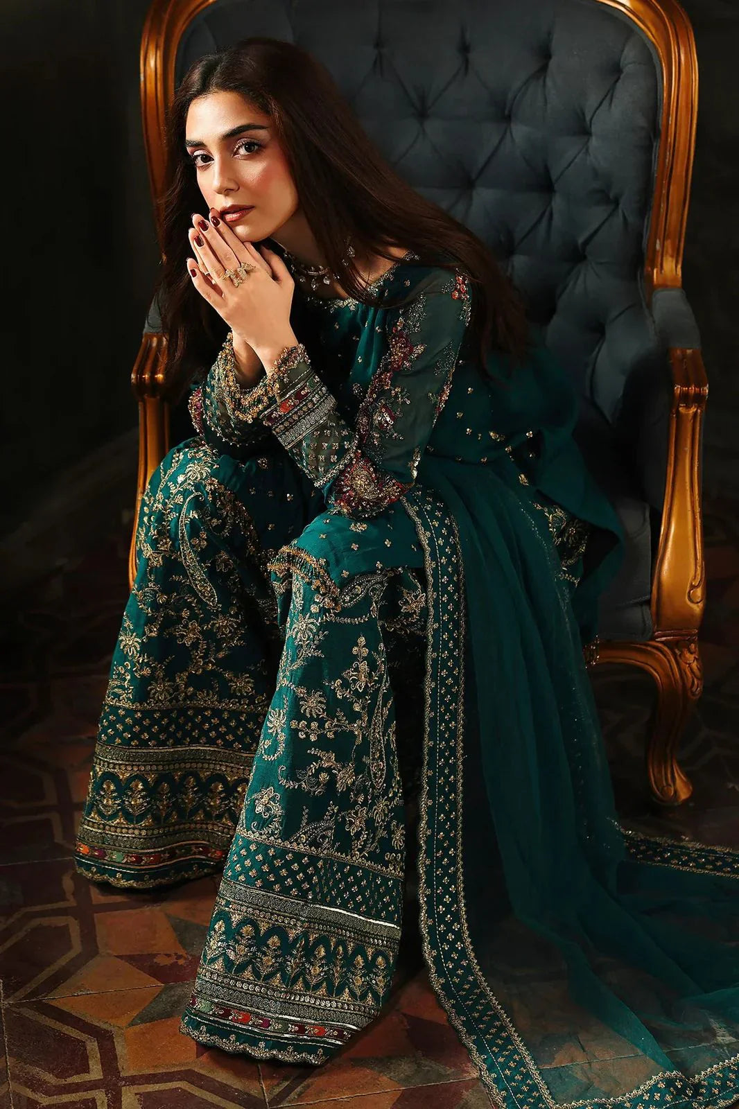 Woman in a traditional teal and gold outfit sitting on an ornate chair.