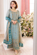 Woman in a light blue embroidered traditional outfit standing in front of floral decorations.