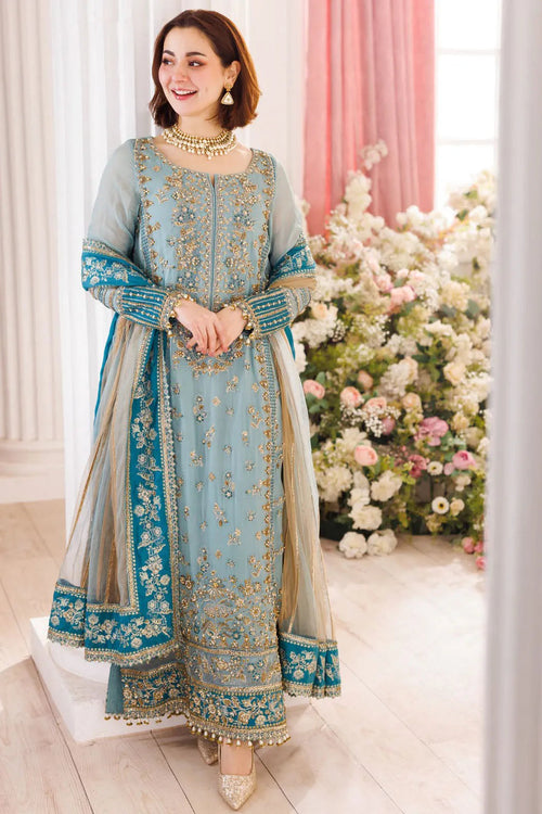 Woman in a light blue embroidered traditional outfit standing in front of floral decorations.
