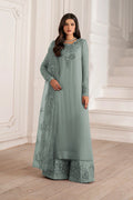 A woman modeling a sage green traditional Indian outfit with matching dupatta, featuring intricate floral embroidery on the neckline and along the borders of the kurta and wide-leg pants, set against a white classical interior background.