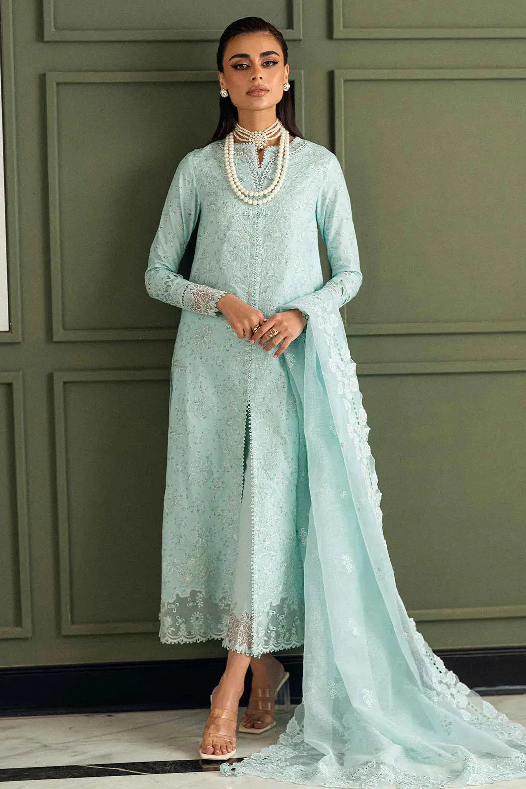 Woman in a light blue embroidered outfit with a matching dupatta against a green paneled wall.